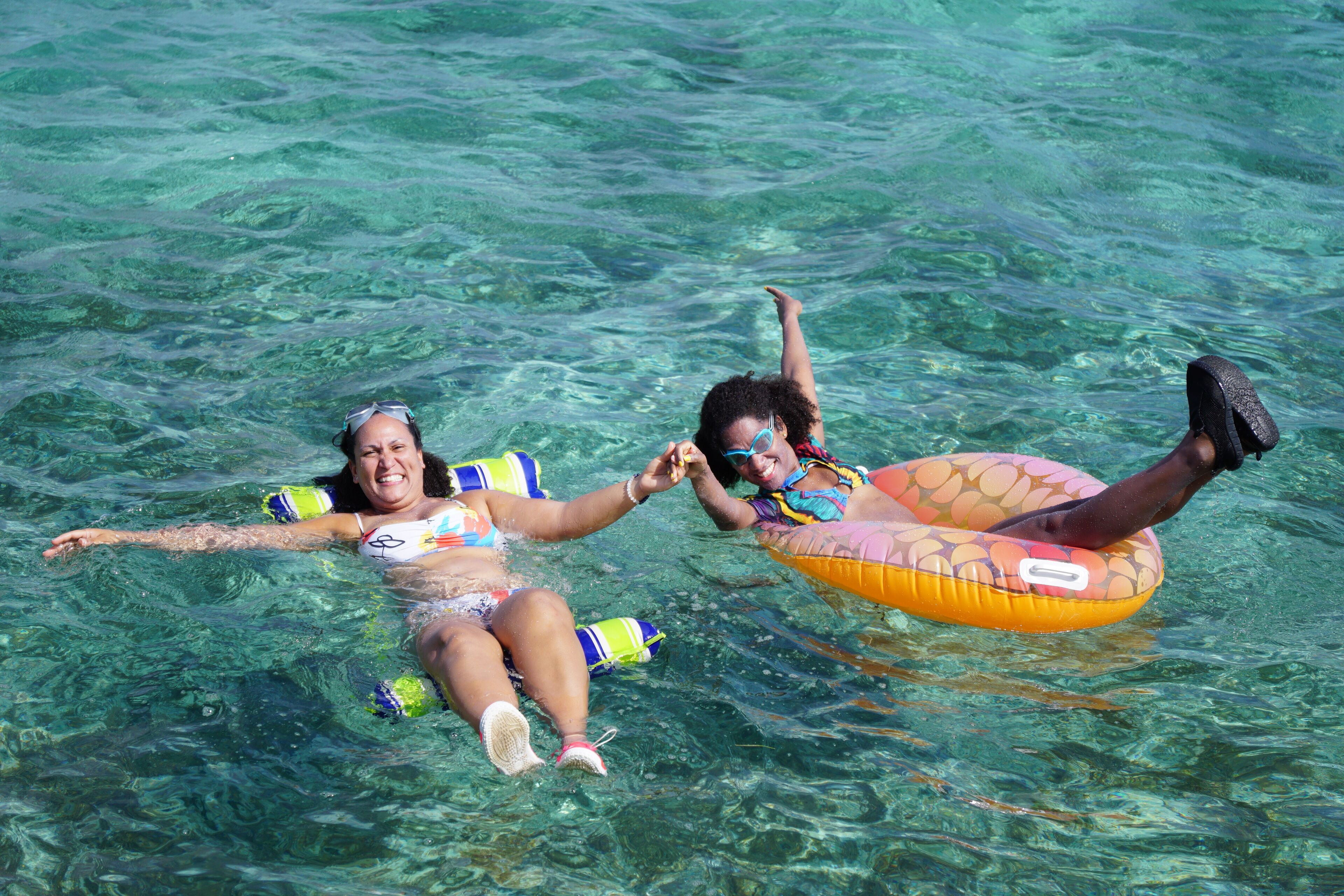Two people floating on a clear blue sea, using inflatable rings.