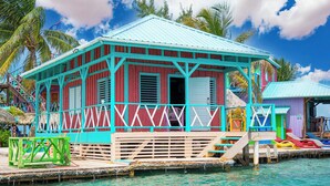A colorful wooden house with a turquoise roof, situated on a dock with clear turquoise water. - King Lewey's Island Resort (Placencia)