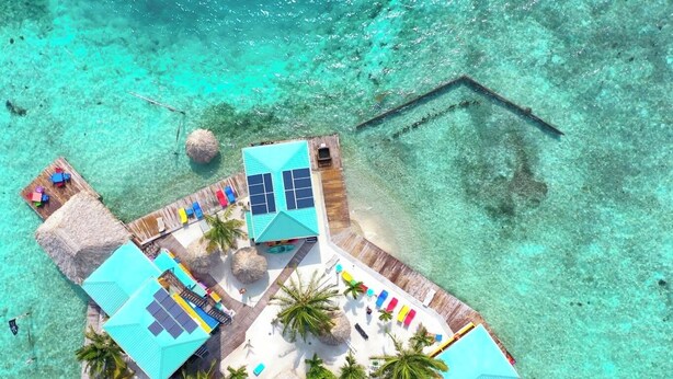 An aerial view of a resort with multiple buildings, a wooden pier, and clear turquoise waters. - King Lewey's Island Resort (Placencia)