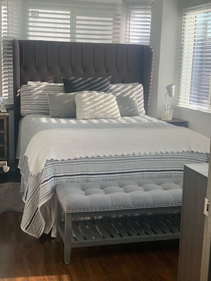 Une chambre à coucher avec un grand lit, une table de chevet avec une lampe et une fenêtre avec des stores.