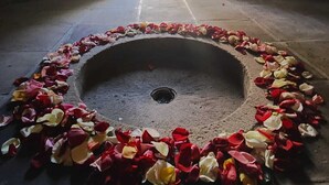 Um corredor de pedra em arco com uma bacia circular de pedra no centro, cercado por pétalas de rosa espalhadas.