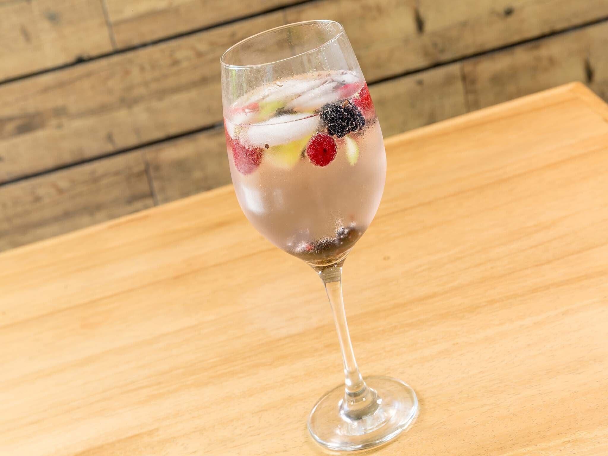 Un vaso de bebida transparente con rodajas de fruta sobre una superficie de madera.