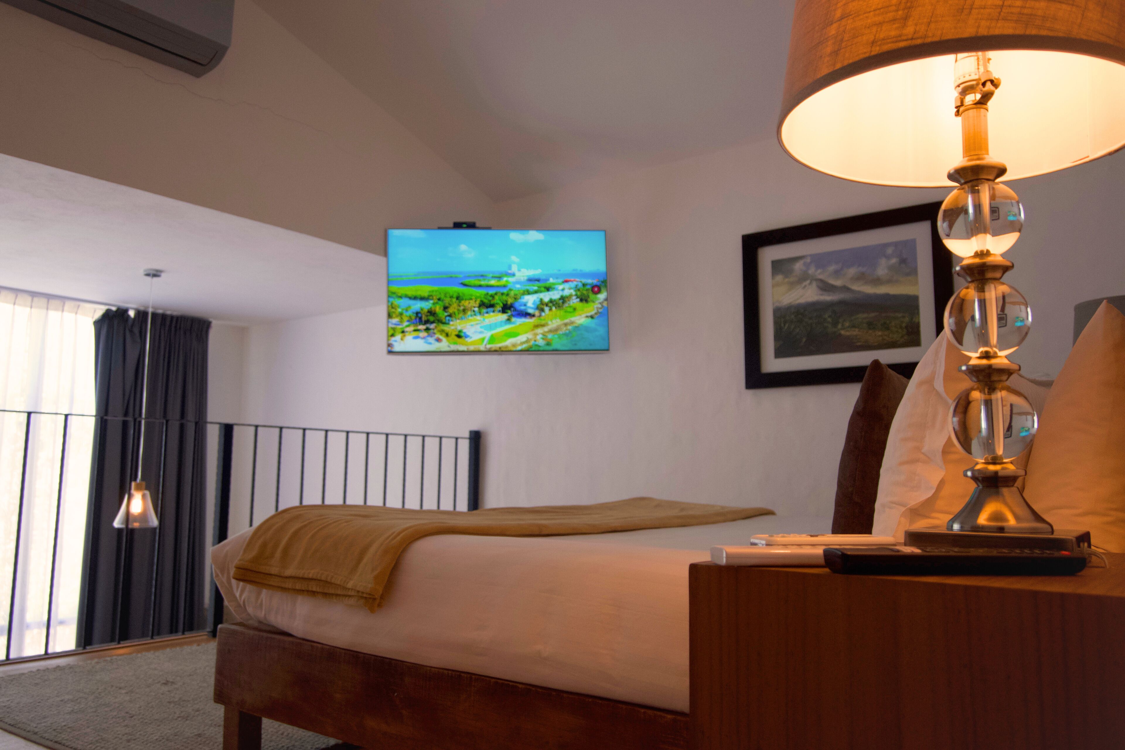 A hotel room with a bed, a television mounted on the wall, a lamp on the bedside table, and a window with curtains.