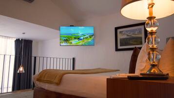 A hotel room with a bed, a television mounted on the wall, a lamp on the bedside table, and a window with curtains.