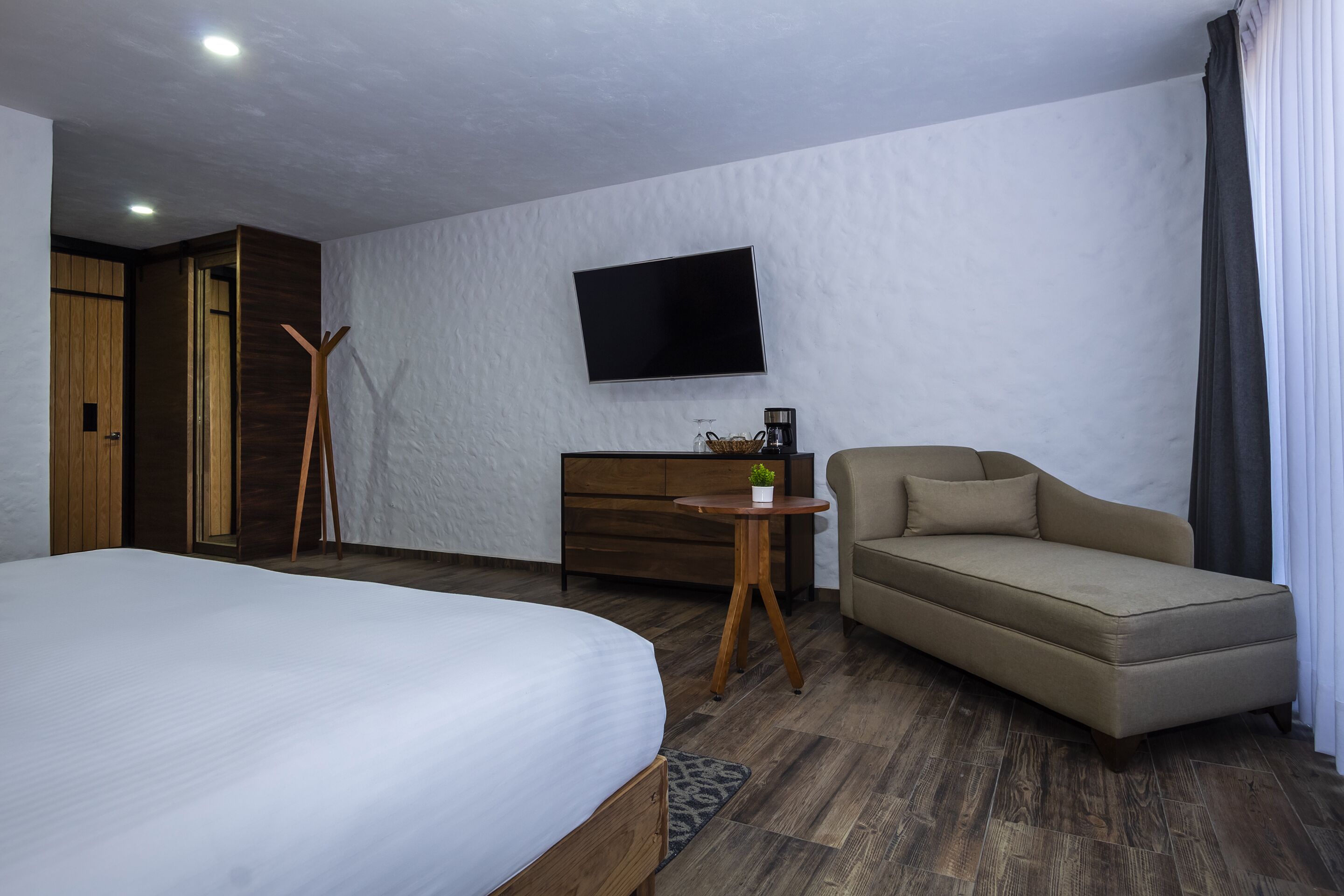 A hotel room with a bed, a sofa, a TV, a dresser, and a wooden floor.