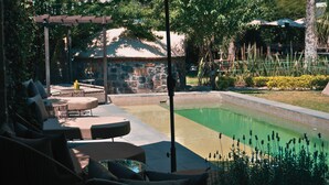 Uma área de piscina com espreguiçadeiras, um pérgola e um muro de pedra ao fundo.