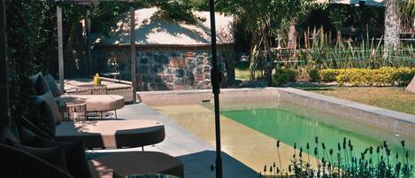 A pool area with lounge chairs, a pergola, and a stone wall in the background.