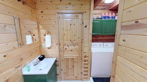 LâintĂ©rieur dâune cabane en bois, avec une porte en bois, un lavabo Ă©quipĂ© de produits de toilette et un lave-linge.