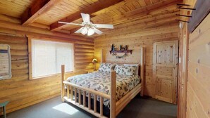 A wooden cabin bedroom with a bed, a ceiling fan, a window, and a door. - Pine Mt Lodge* 6Br, 3.5Ba, Wifi, 42 Miles to YNP (Island Park)