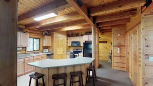A wooden cabin interior with a kitchen area featuring a central island with stools, wooden cabinets, a microwave, a stove, and a refrigerator. - Pine Mt Lodge* 6Br, 3.5Ba, Wifi, 42 Miles to YNP (Island Park)