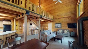 A wooden cabin interior with a dining area, sofa, and fireplace. - Pine Mt Lodge* 6Br, 3.5Ba, Wifi, 42 Miles to YNP (Island Park)