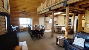 A log cabin interior with a dining area, kitchen, and a living room with a couch and a lamp. - Pine Mt Lodge* 6Br, 3.5Ba, Wifi, 42 Miles to YNP (Island Park)