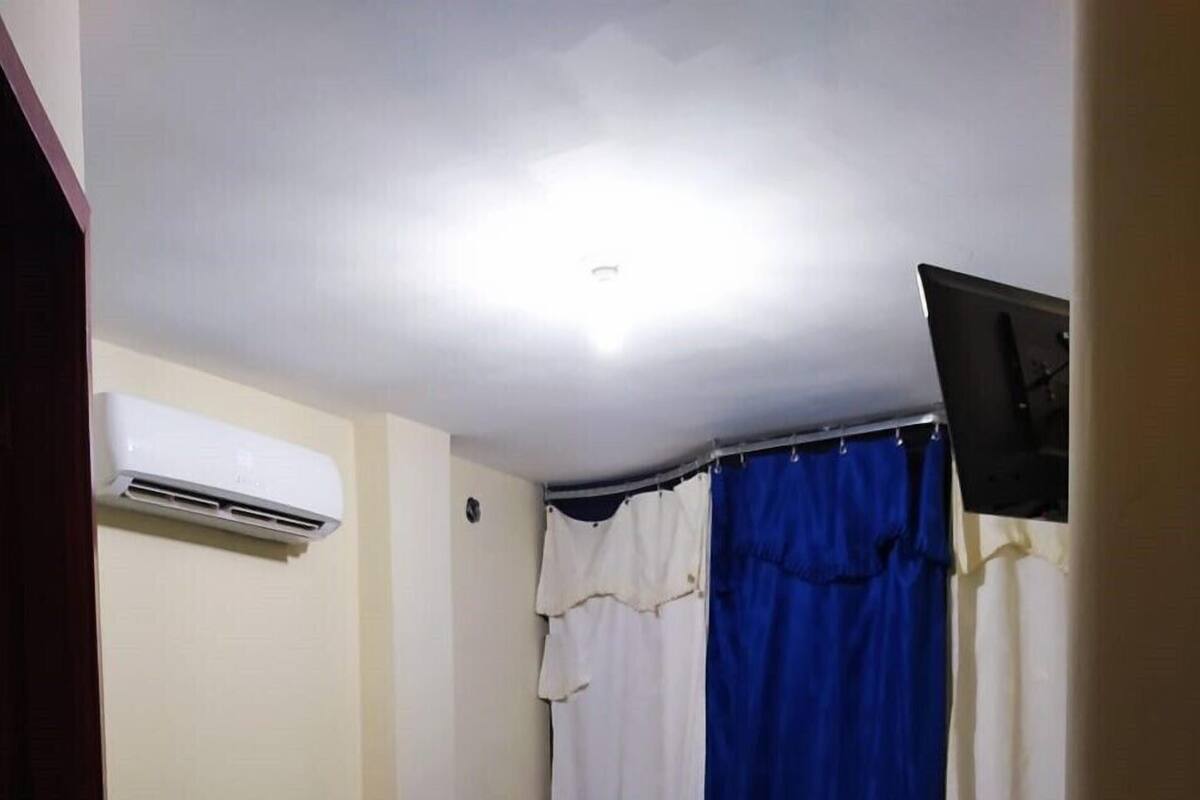 A hotel room with two beds, a flat-screen TV, an air conditioner, and a nightstand with a phone and water bottles.