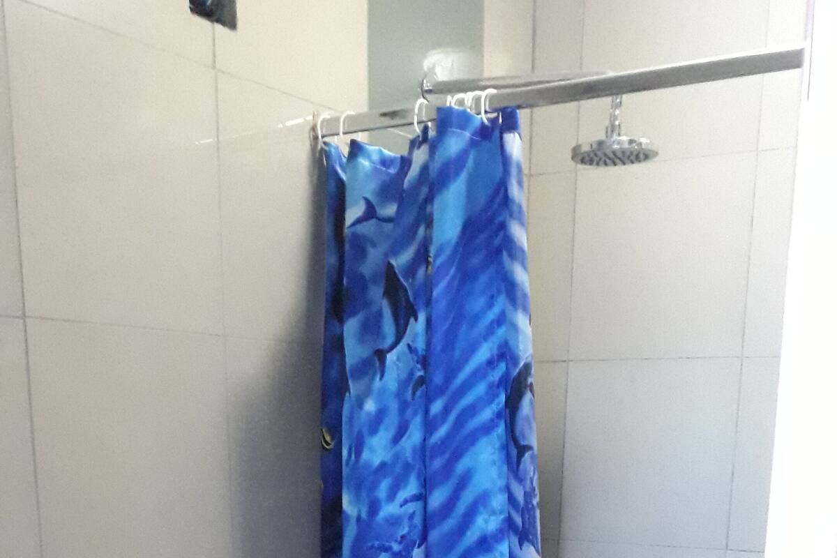 A bathroom with a white toilet, a shower curtain with a blue pattern, and tiled walls.
