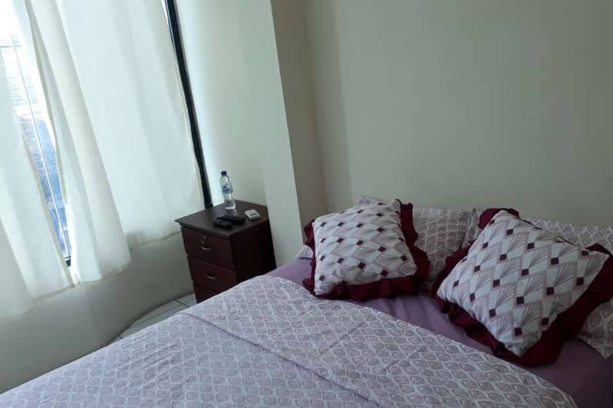 A bedroom with a bed, pillows, a nightstand, and a window with curtains.