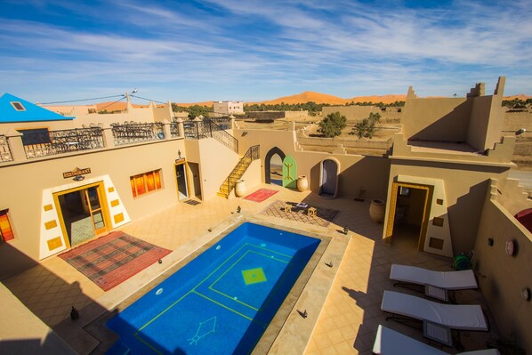 A rooftop pool area with lounge chairs, a restaurant, and a view of the desert landscape.