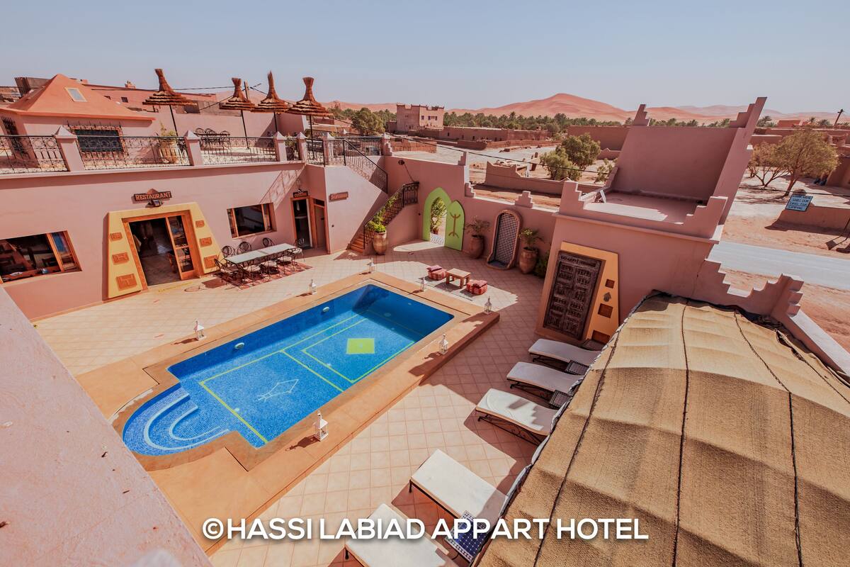 A rooftop pool area with lounge chairs and a sign for the Chassi Labiad Apart Hotel.