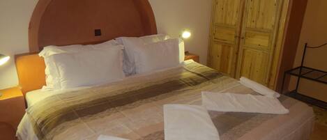 Una habitación de hotel con una cama grande, un armario de madera y dos lámparas de noche.