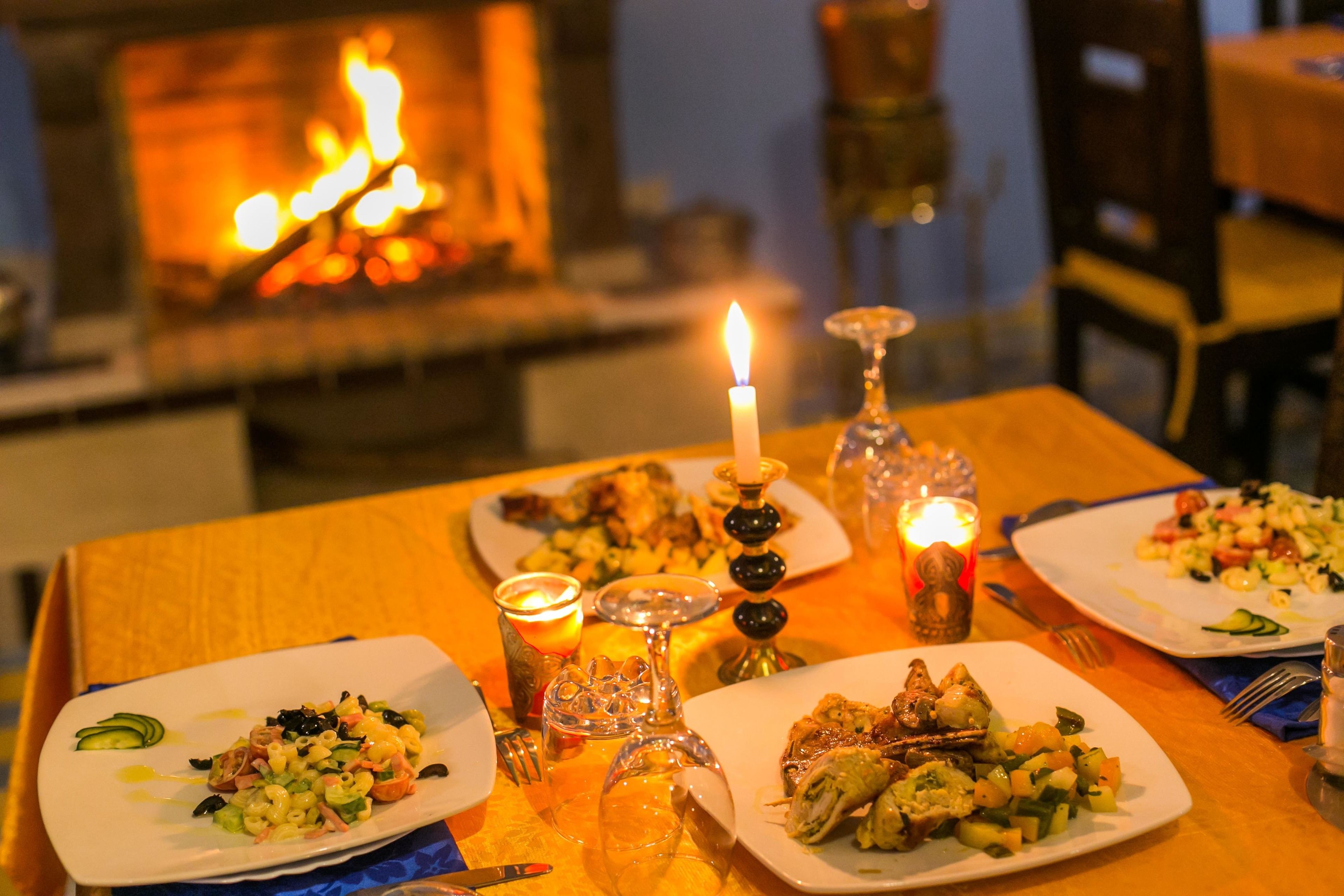 A dining table with plates of food, candles, and a lit fireplace in the background.