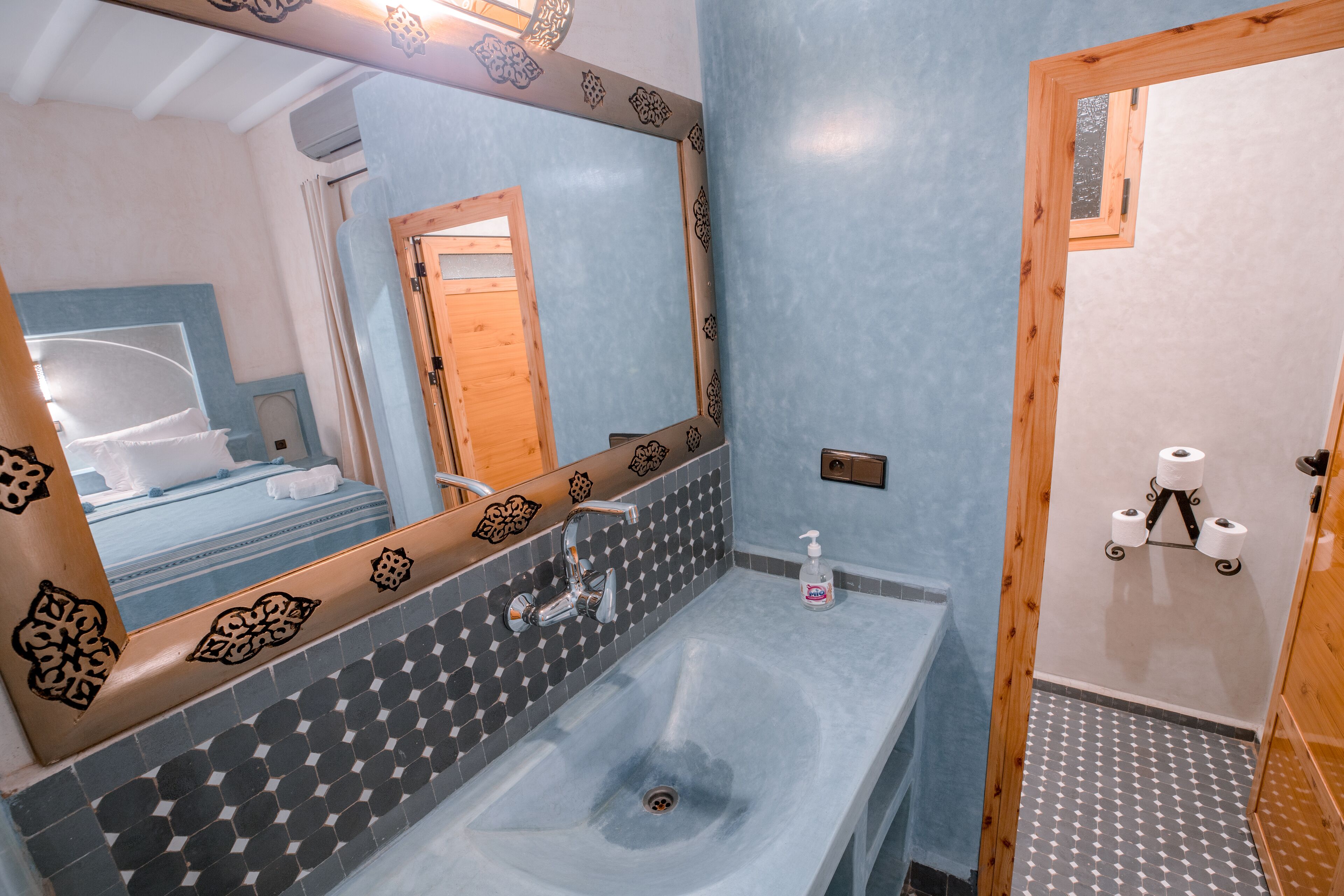 Un baño con lavamanos, espejo y dispensador de papel higiénico.