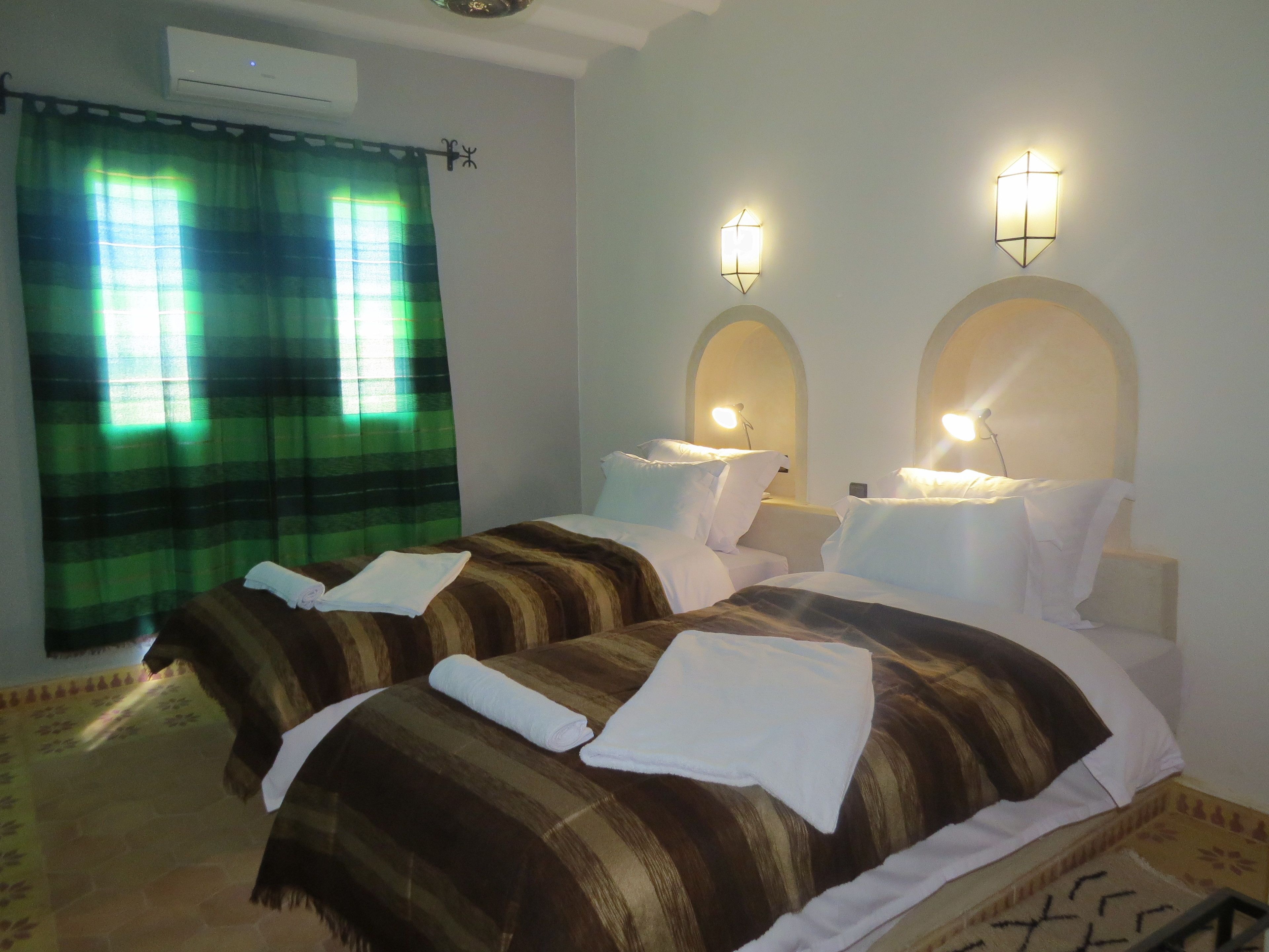 A hotel room with two beds, a green curtain, and wall-mounted lights.