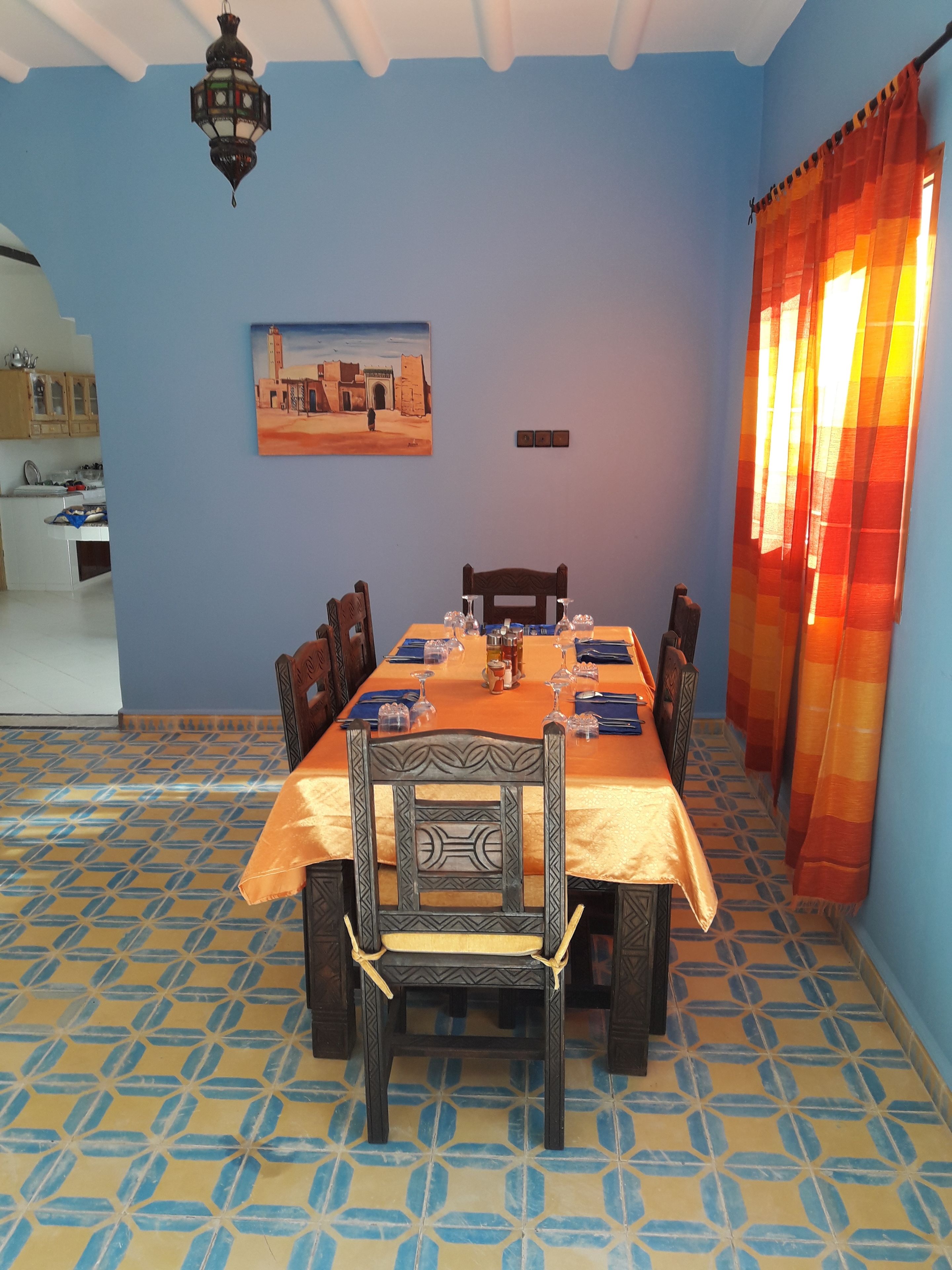 Een eetgedeelte met een tafel voor zes personen, stoelen, een schilderij aan de muur en een vloer met patroon.