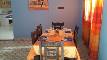 A dining area with a table set for six, chairs, a painting on the wall, and a patterned floor.