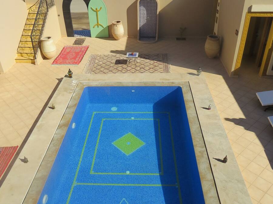 Zona de piscina en la azotea con suelo azul, una pequeña mesa y un diseño de mosaicos decorativos.