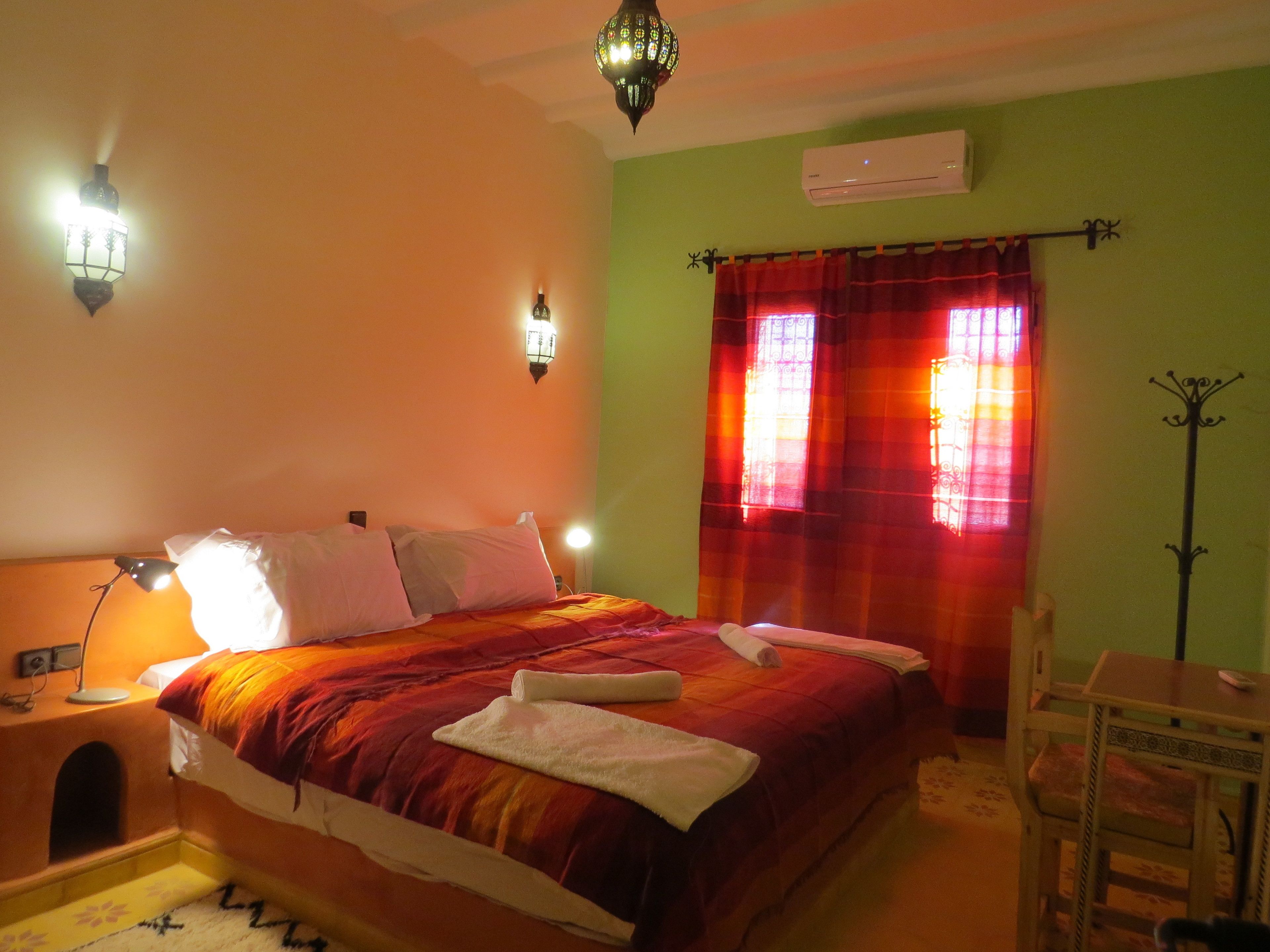 A bedroom with a bed, bedside lamps, a chair, a table, and a window with curtains.