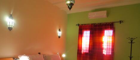 Un dormitorio con cama, lámparas de noche, una silla, una mesa y una ventana con cortinas.
