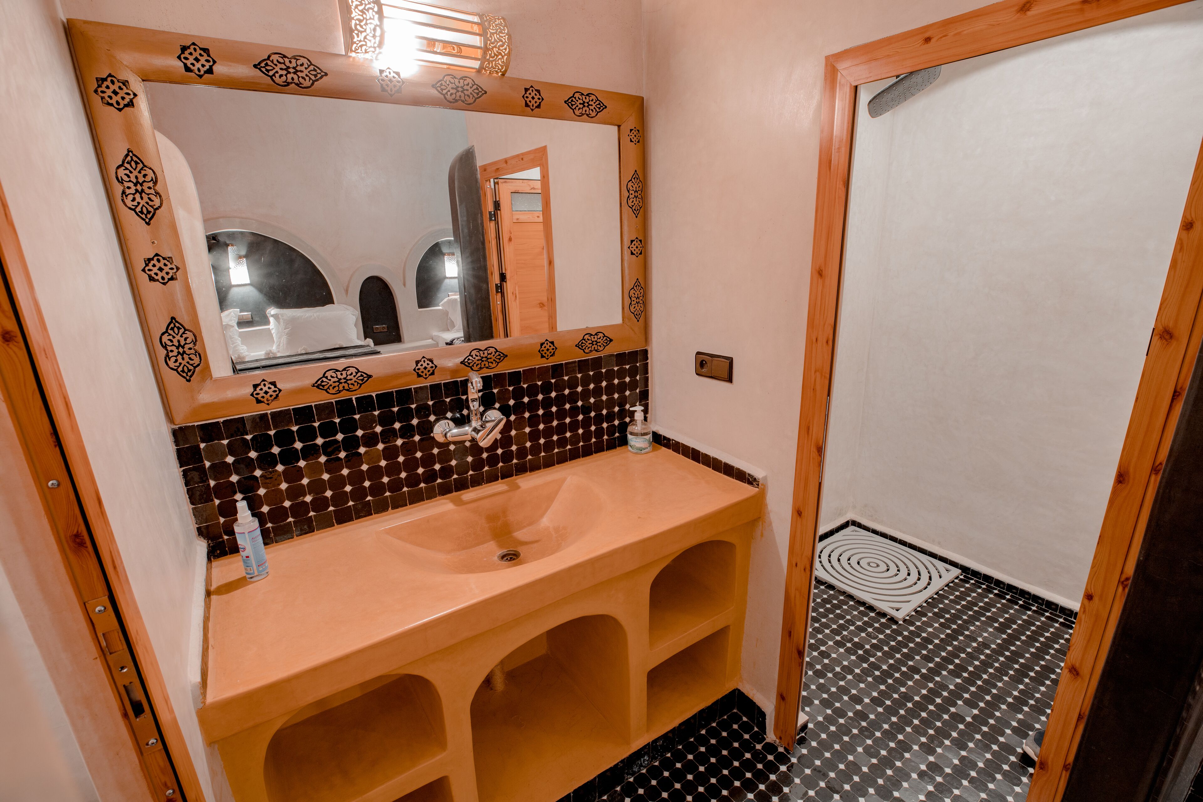 Ein Badezimmer mit Holzwaschtisch, einem Waschbecken, einem Spiegel mit dekorativem Rahmen und einem gemusterten Boden.
