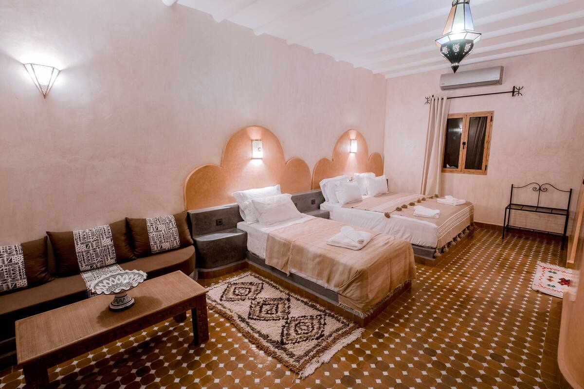 A hotel room with two beds, a sofa, a small table, and patterned flooring.