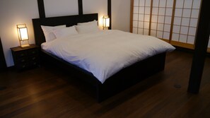 A neatly made bed with white linens in a room with wooden flooring and a dark headboard. There are two bedside tables with lamps on either side of the bed.