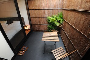 A compact room with a bed, a small table, a potted plant, and a pair of sandals on the floor.