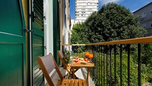 A balcony with a wooden table set with food and drinks, a chair, and a view of a building and trees. - Sailor Boutique Rooms (Split)