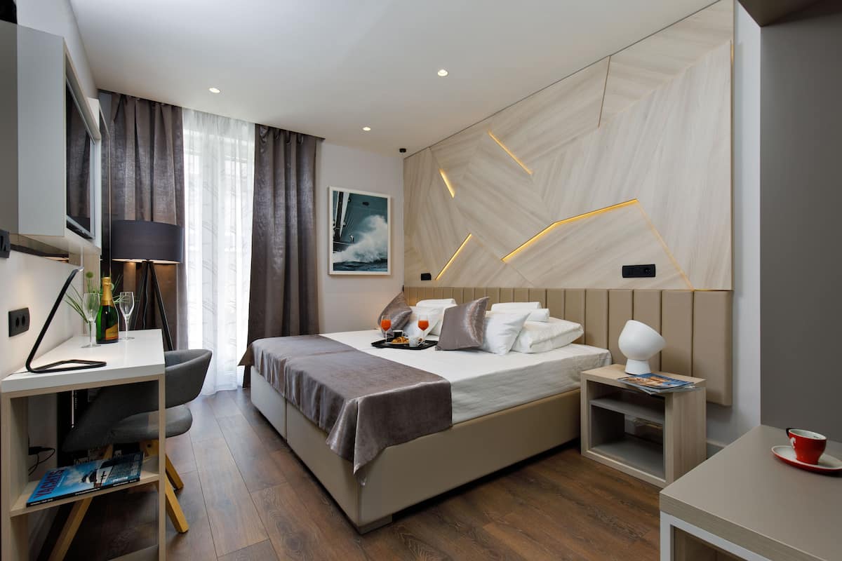 A modern hotel room with a bed, bedside table, desk, and chair.