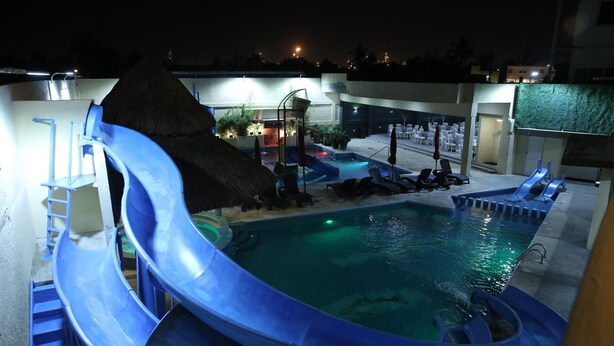 A pool area with a blue slide, lounge chairs, and a thatched-roof structure. - Hotel Miramar Inn (Ciudad Madero)
