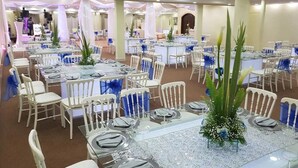 A banquet hall with multiple round tables set with white chairs and blue sashes, featuring a central floral arrangement. - Hotel Miramar Inn (Ciudad Madero)