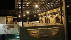 An outdoor seating area with tables and chairs, a covered section with a curved roof, and a building with arched windows in the background. - Hotel Miramar Inn (Ciudad Madero)