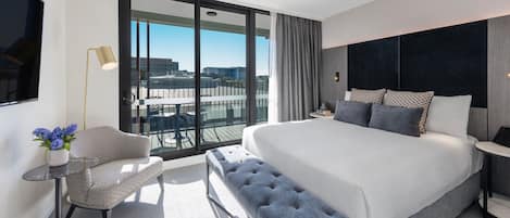 Une chambre d’hôtel moderne dotée d’un grand lit, d’un coin salon et d’un balcon offrant une vue sur la ville.