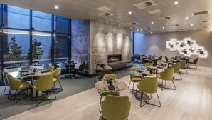 Un restaurante moderno con mesas redondas y sillas amarillas, una chimenea y ventanas amplias.