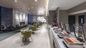 A modern dining area with multiple tables and chairs, a buffet with various food options, and a decorative light installation on the wall.