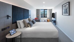 Una habitación de hotel moderna con una cama grande, una mesita auxiliar pequeña, un televisor y una ventana con vistas a la ciudad.