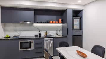 Une cuisine moderne avec des meubles gris, un plan de travail blanc, un four encastré, un lave-vaisselle et un petit réfrigérateur.