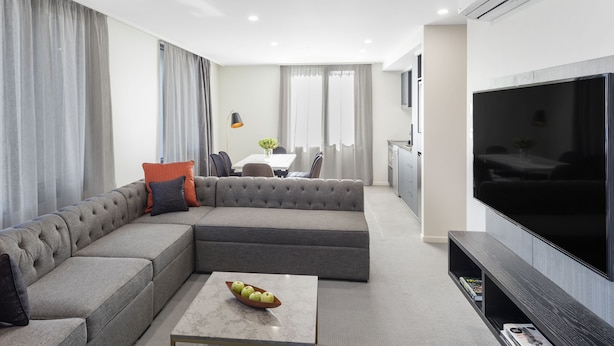 Una sala moderna con un sofá modular, un televisor de pantalla plana y un comedor al fondo.