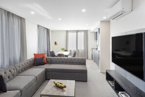 A modern living room with a sectional sofa, a flat-screen TV, and a dining area in the background. - Deco Hotel (Braddon)