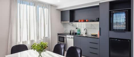 A modern kitchen with grey cabinets, a black refrigerator, and a dining area with a white table and chairs.