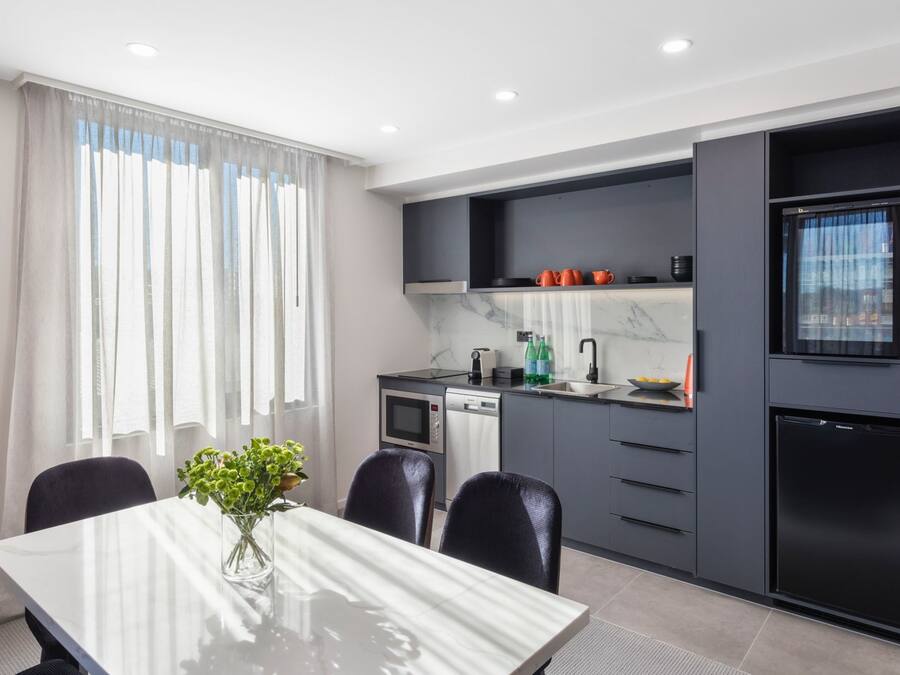 A modern kitchen with grey cabinets, a black refrigerator, and a dining area with a white table and chairs.