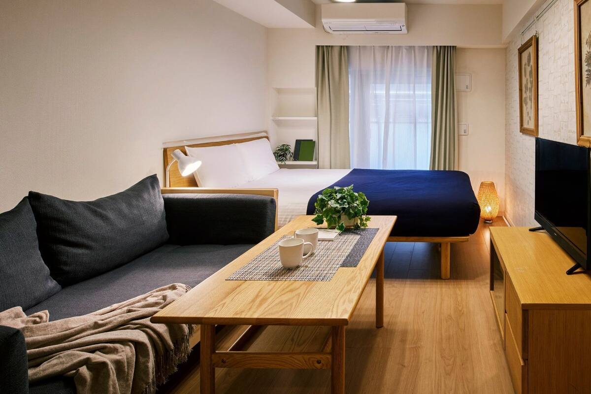 A modern, well-lit hotel room with a bed, sofa, and a small table with a plant and two mugs.