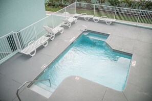 Una piscina rettangolare con recinzione bianca e lettini attorno.